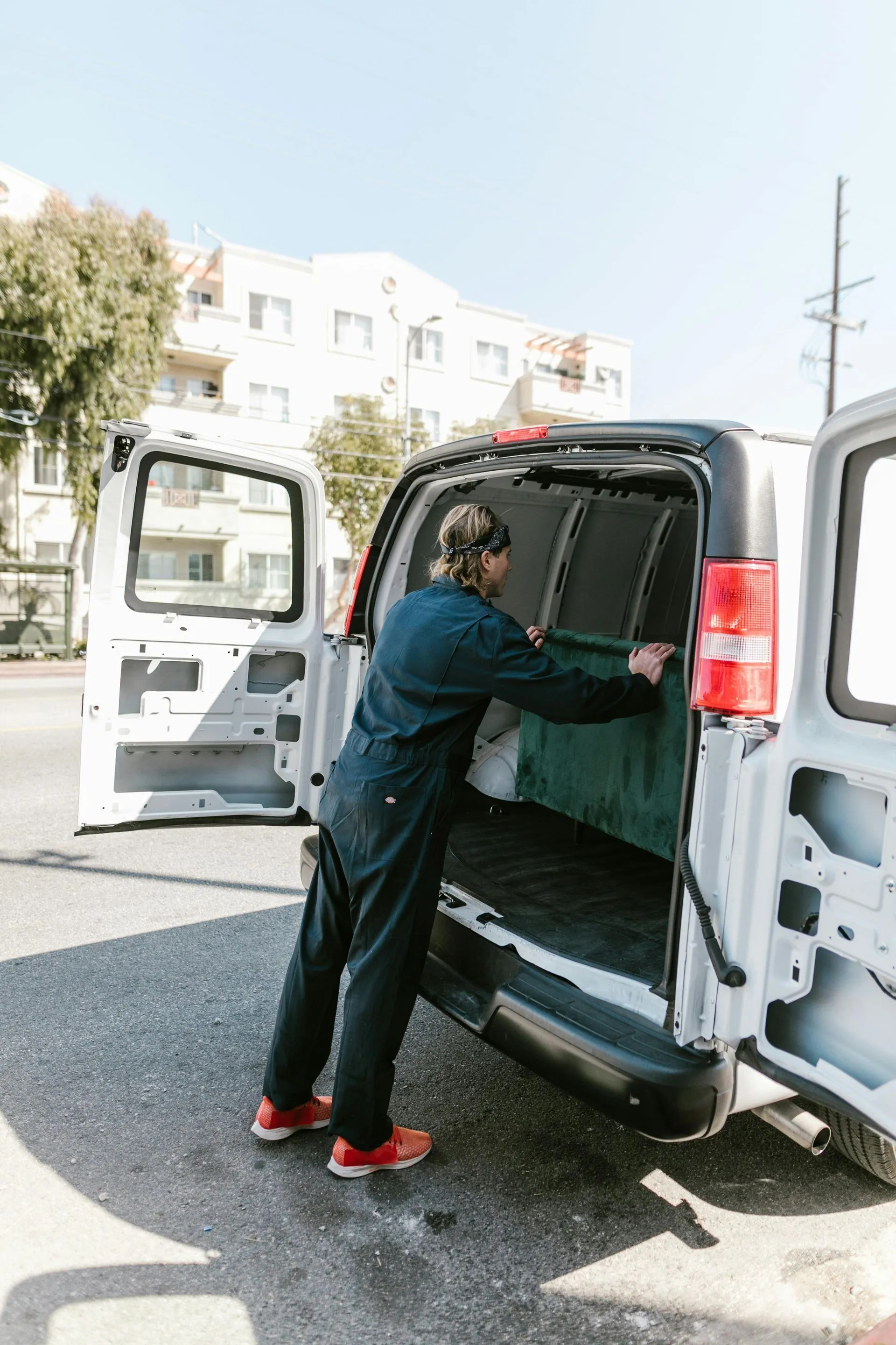 Mover loading a padded bundle into the back of a white cargo van on a city street.