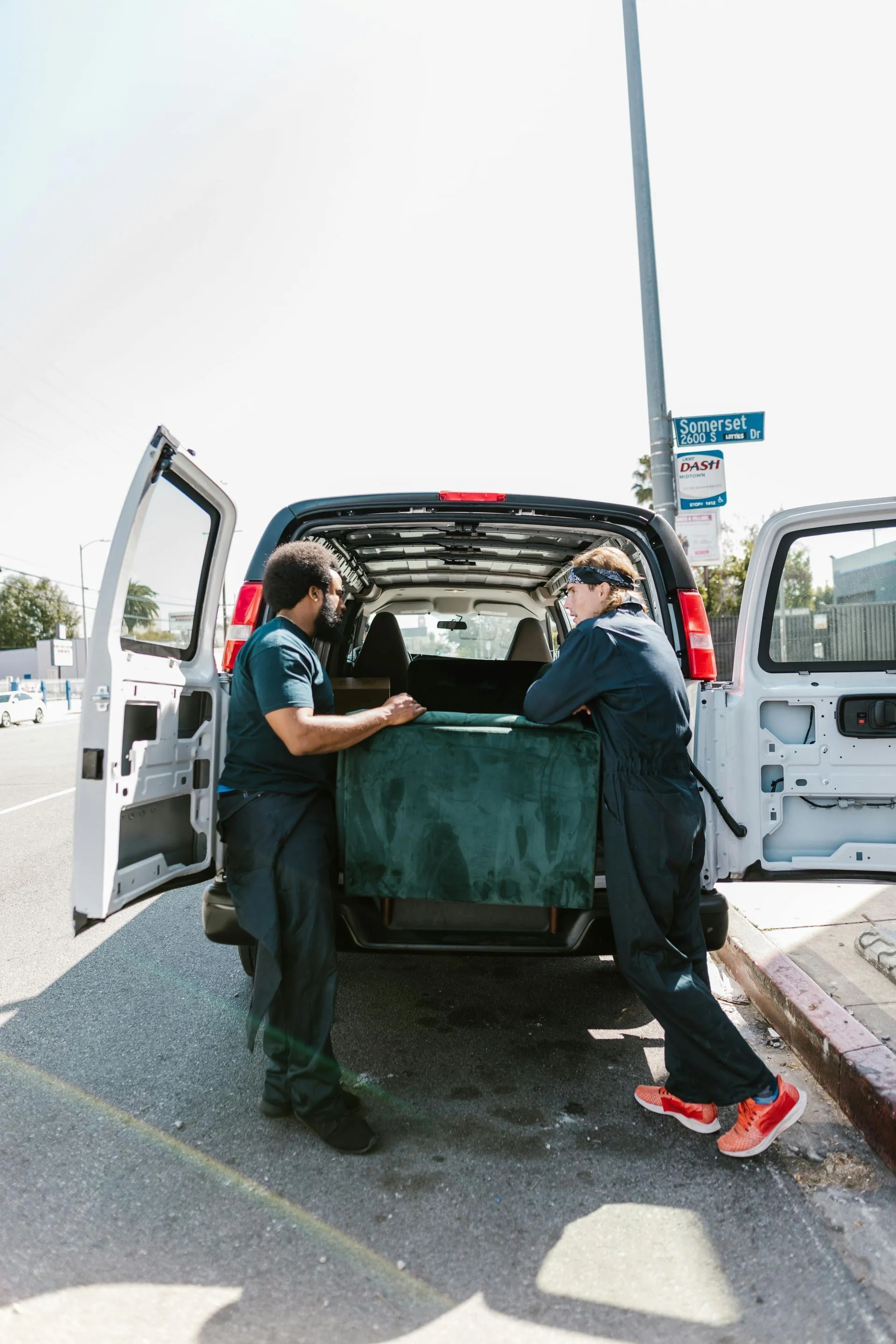 Two movers lifting a blanket-wrapped item into the back of a white van.