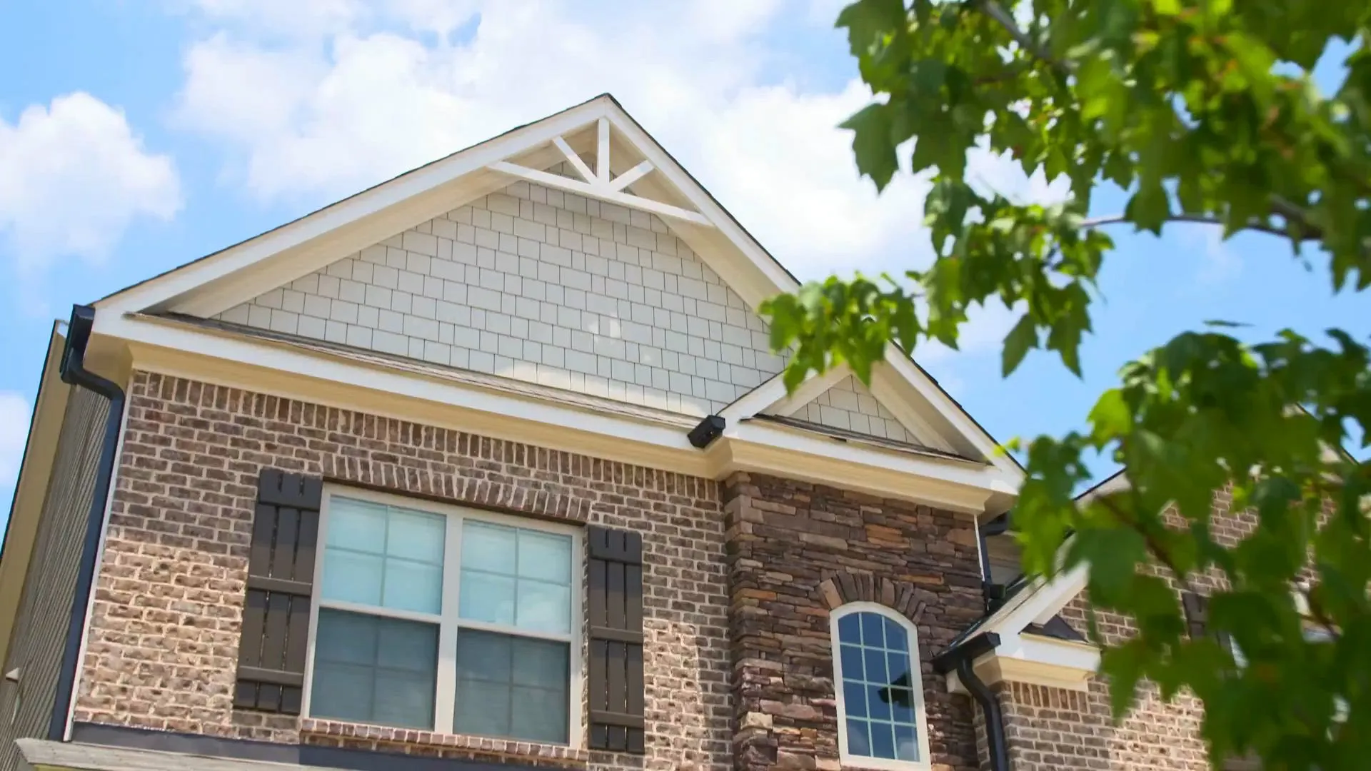 Two-story brick home with a gabled roof and dark shutters under a blue sky.